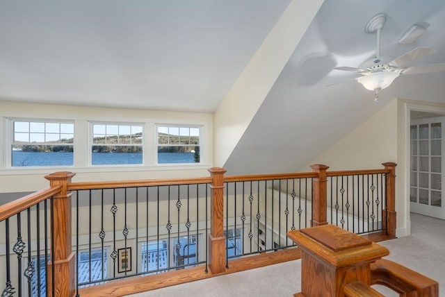 hallway with vaulted ceiling, a water view, a healthy amount of sunlight, and light carpet