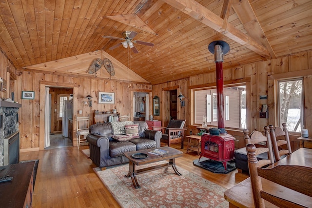 living room with wooden ceiling, wooden walls, lofted ceiling with beams, and a wood stove