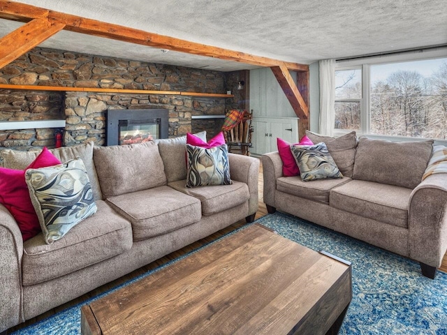 living room featuring beamed ceiling, a stone fireplace, and a textured ceiling