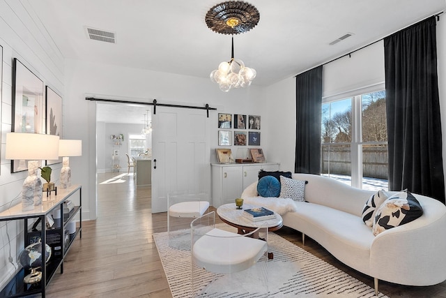 living room with a notable chandelier, a barn door, and light wood-type flooring