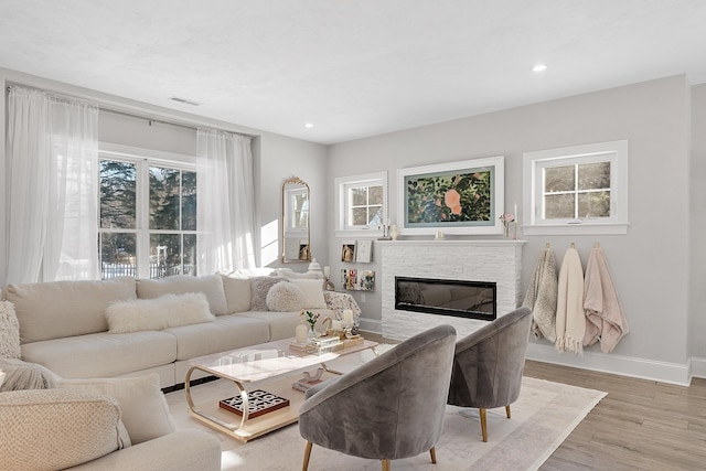 living room with plenty of natural light, a stone fireplace, and light hardwood / wood-style floors