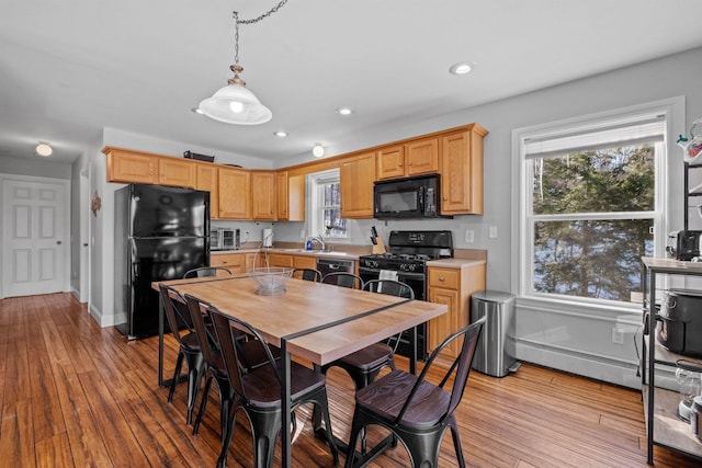 kitchen featuring light brown cabinetry, sink, decorative light fixtures, light hardwood / wood-style flooring, and black appliances