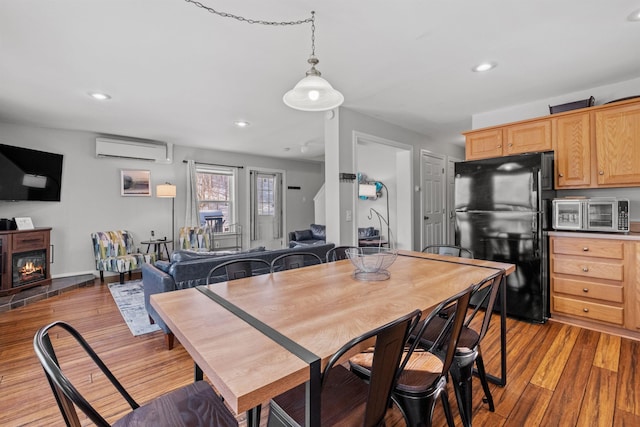 dining area with a wall mounted AC and light hardwood / wood-style floors