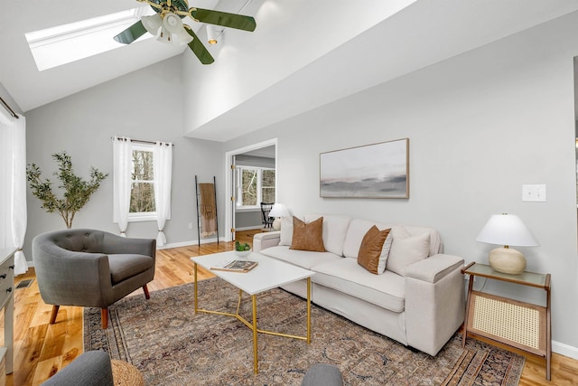 living room with hardwood / wood-style flooring, a skylight, high vaulted ceiling, and ceiling fan