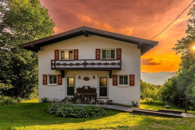 back house at dusk featuring a lawn