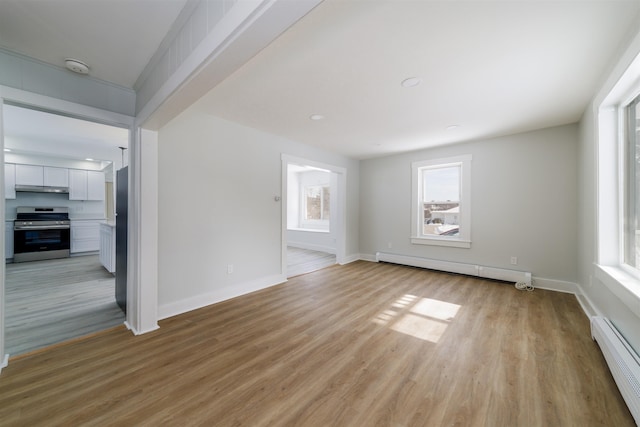 unfurnished living room featuring a baseboard heating unit, a wealth of natural light, and light hardwood / wood-style floors