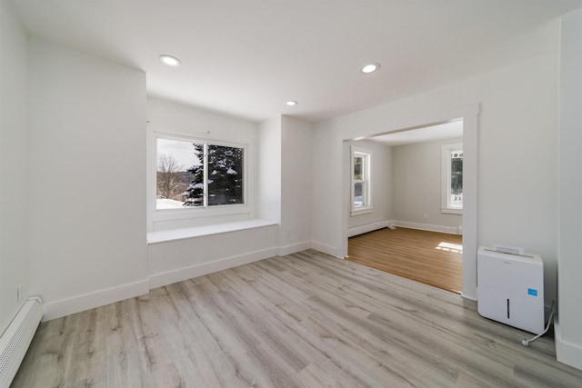 spare room featuring a baseboard heating unit, plenty of natural light, and light hardwood / wood-style floors