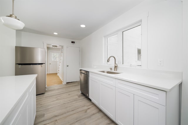 kitchen featuring pendant lighting, sink, appliances with stainless steel finishes, white cabinetry, and light wood-type flooring