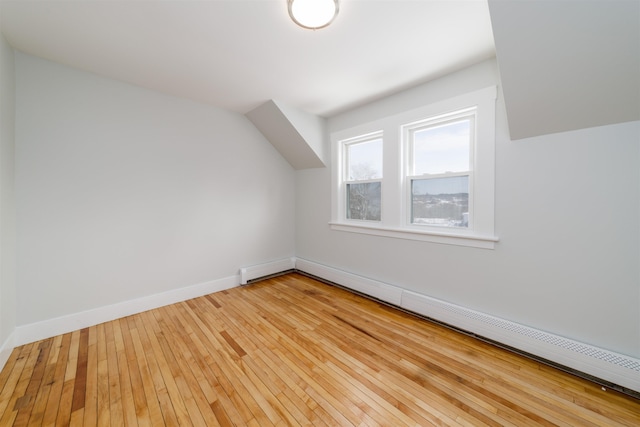 additional living space featuring a baseboard radiator, lofted ceiling, and light hardwood / wood-style floors