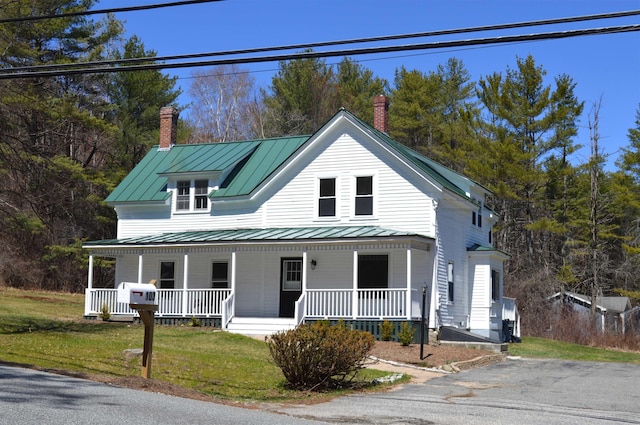 farmhouse-style home featuring covered porch, a chimney, and a standing seam roof