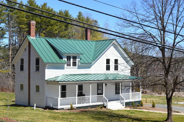 view of front of property with a front yard, a chimney, a standing seam roof, covered porch, and metal roof