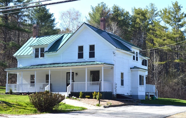 view of front of home with covered porch, metal roof, a chimney, and a standing seam roof