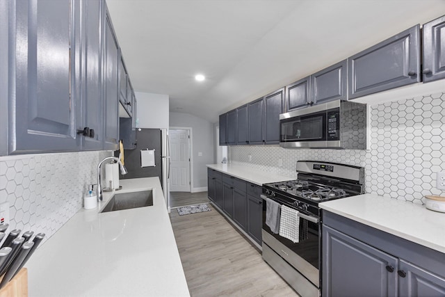 kitchen featuring vaulted ceiling, appliances with stainless steel finishes, sink, backsplash, and light hardwood / wood-style floors