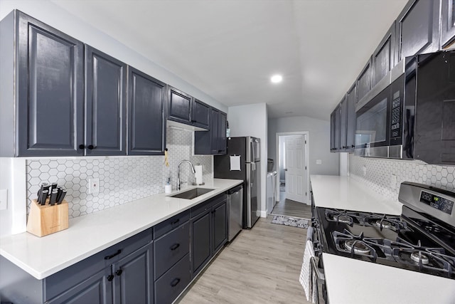 kitchen with lofted ceiling, sink, appliances with stainless steel finishes, tasteful backsplash, and light wood-type flooring