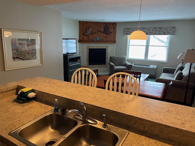 kitchen with sink, a textured ceiling, an AC wall unit, a tile fireplace, and pendant lighting