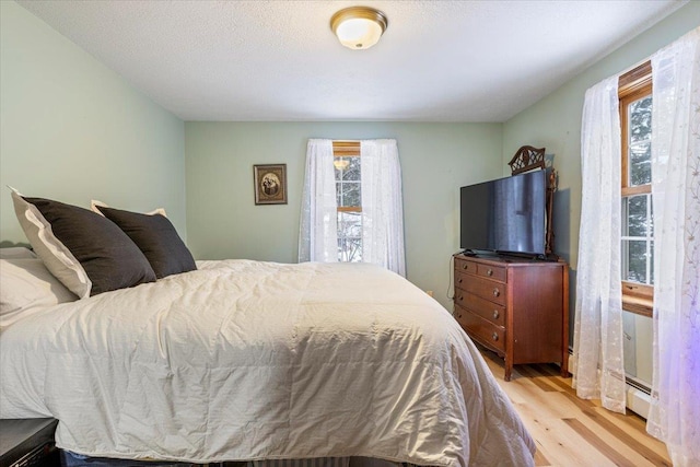 bedroom with multiple windows, a baseboard radiator, light hardwood / wood-style floors, and a textured ceiling