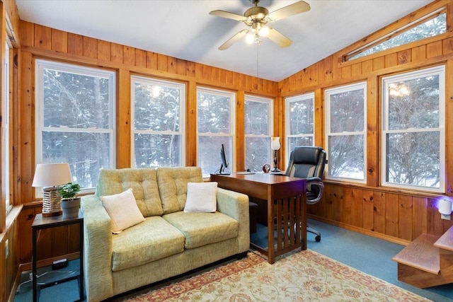 carpeted office featuring vaulted ceiling, ceiling fan, and wood walls