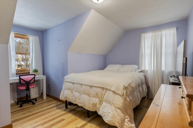 bedroom with vaulted ceiling, a textured ceiling, and light hardwood / wood-style floors