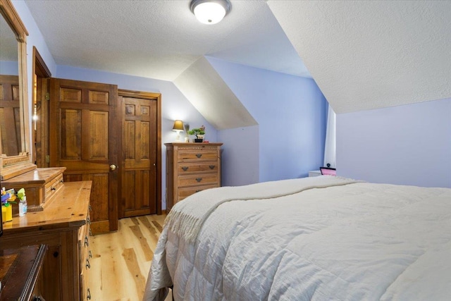 bedroom with vaulted ceiling, a textured ceiling, and light wood-type flooring