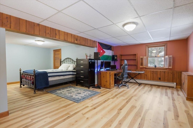 bedroom featuring wood walls, a drop ceiling, light hardwood / wood-style floors, and a baseboard heating unit