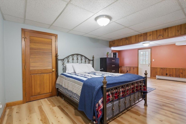 bedroom featuring a baseboard radiator, wood walls, a paneled ceiling, and light wood-type flooring