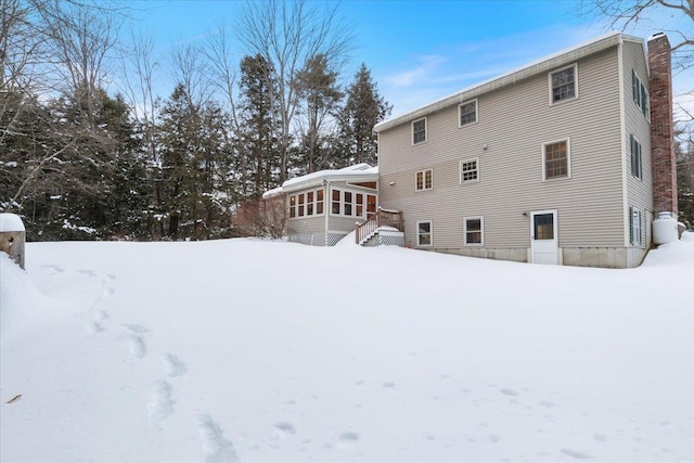 snow covered back of property with a sunroom