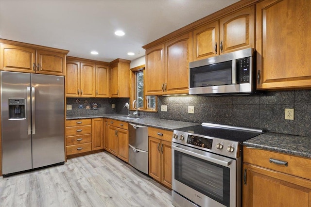 kitchen featuring appliances with stainless steel finishes, tasteful backsplash, sink, dark stone counters, and light hardwood / wood-style floors