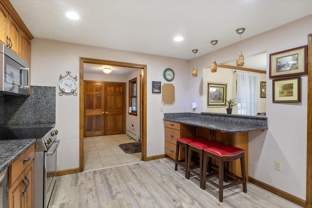 kitchen with appliances with stainless steel finishes, a baseboard radiator, a breakfast bar area, hanging light fixtures, and light hardwood / wood-style floors