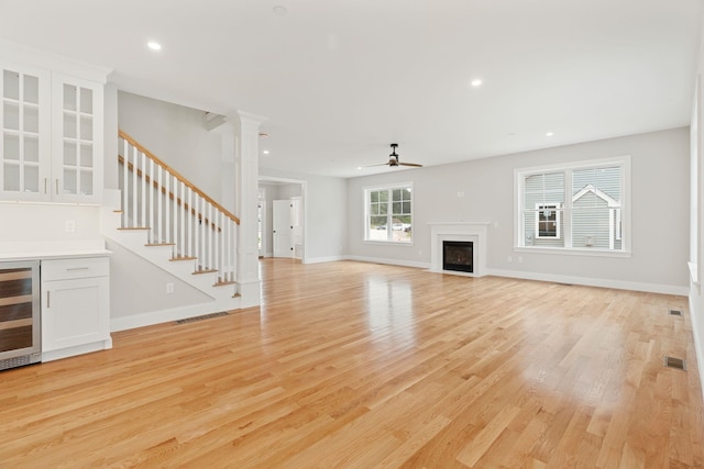 unfurnished living room featuring ornate columns, ceiling fan, beverage cooler, and light hardwood / wood-style floors