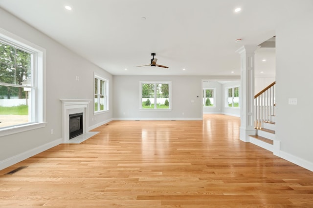 unfurnished living room featuring ornate columns, ceiling fan, a high end fireplace, and light wood-type flooring