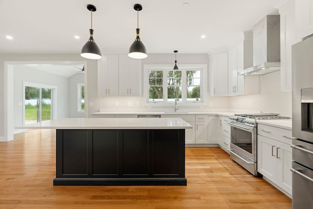 kitchen with wall chimney exhaust hood, sink, white cabinetry, decorative light fixtures, and appliances with stainless steel finishes