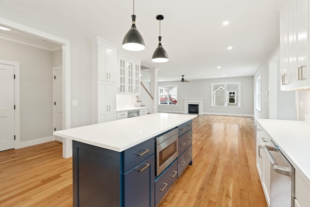 kitchen with pendant lighting, blue cabinets, white cabinetry, light hardwood / wood-style floors, and stainless steel appliances