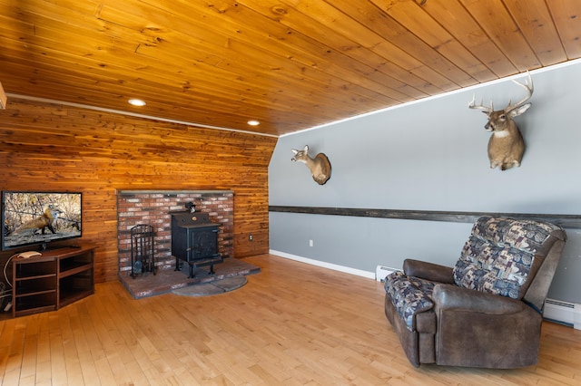 sitting room with light hardwood / wood-style flooring, wood ceiling, a baseboard radiator, and a wood stove