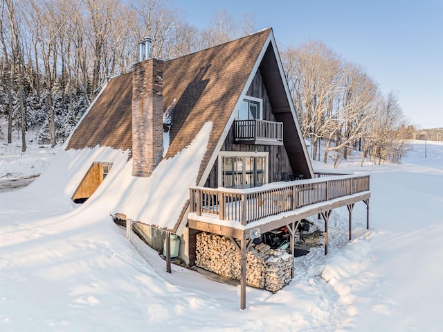 snow covered rear of property featuring a balcony and a deck