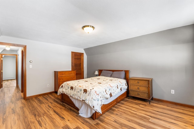 bedroom with vaulted ceiling, a baseboard heating unit, light wood-type flooring, and a closet