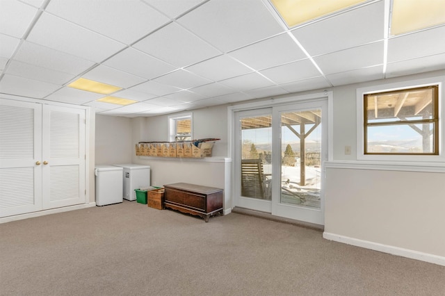 interior space featuring light colored carpet, a drop ceiling, and refrigerator