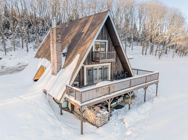 snow covered house featuring a wooden deck and a balcony