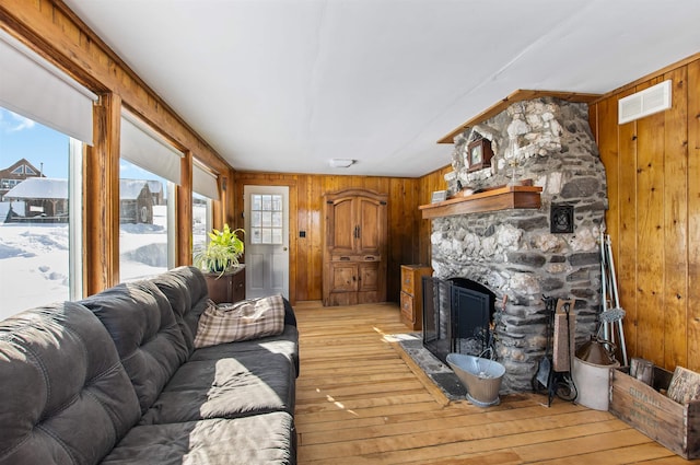 living room with wooden walls, a stone fireplace, and light hardwood / wood-style flooring