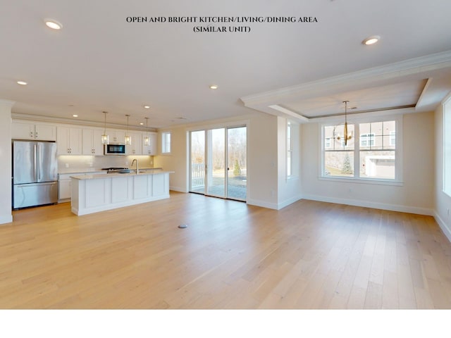 kitchen featuring pendant lighting, stainless steel fridge, white cabinetry, ornamental molding, and a center island with sink