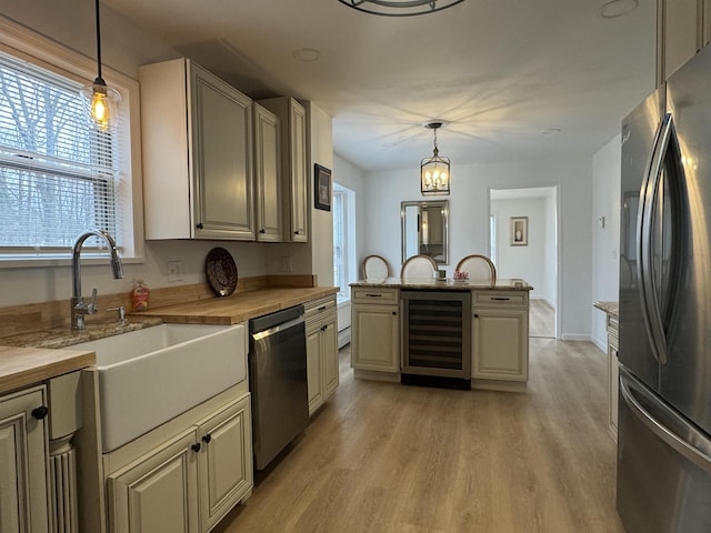 kitchen with pendant lighting, sink, wine cooler, stainless steel appliances, and light hardwood / wood-style flooring