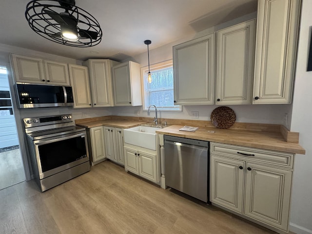 kitchen with sink, wooden counters, light hardwood / wood-style flooring, pendant lighting, and stainless steel appliances