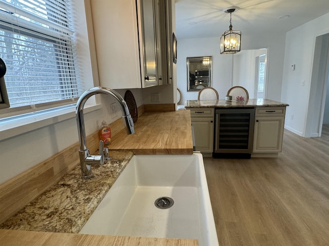 kitchen with sink, light hardwood / wood-style flooring, light stone countertops, decorative light fixtures, and beverage cooler