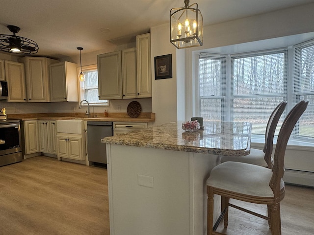 kitchen featuring appliances with stainless steel finishes, a breakfast bar area, light stone counters, and decorative light fixtures