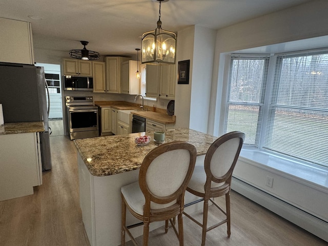 kitchen with pendant lighting, a baseboard radiator, appliances with stainless steel finishes, and light hardwood / wood-style flooring