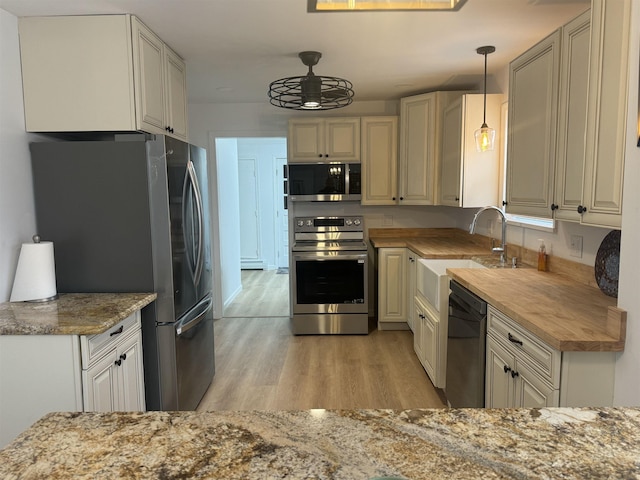 kitchen featuring sink, appliances with stainless steel finishes, wood counters, decorative light fixtures, and light wood-type flooring