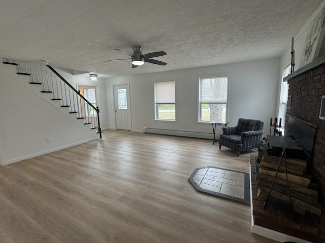 interior space featuring ceiling fan, a baseboard heating unit, a fireplace, and light wood-type flooring