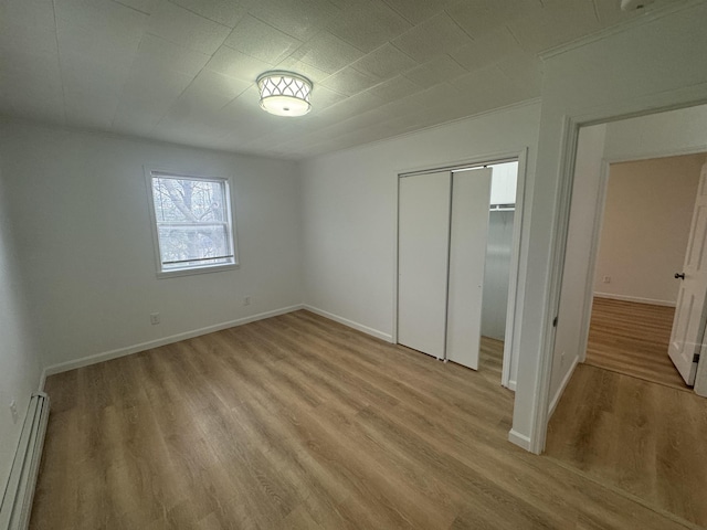 unfurnished bedroom with a baseboard radiator, light hardwood / wood-style floors, and a closet