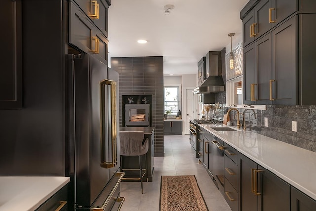 kitchen featuring sink, decorative backsplash, hanging light fixtures, high end appliances, and wall chimney range hood