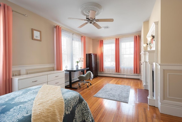 bedroom with ceiling fan, a baseboard heating unit, and light wood-type flooring