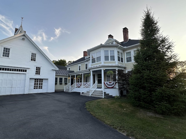 victorian-style house featuring a porch, a garage, and a lawn